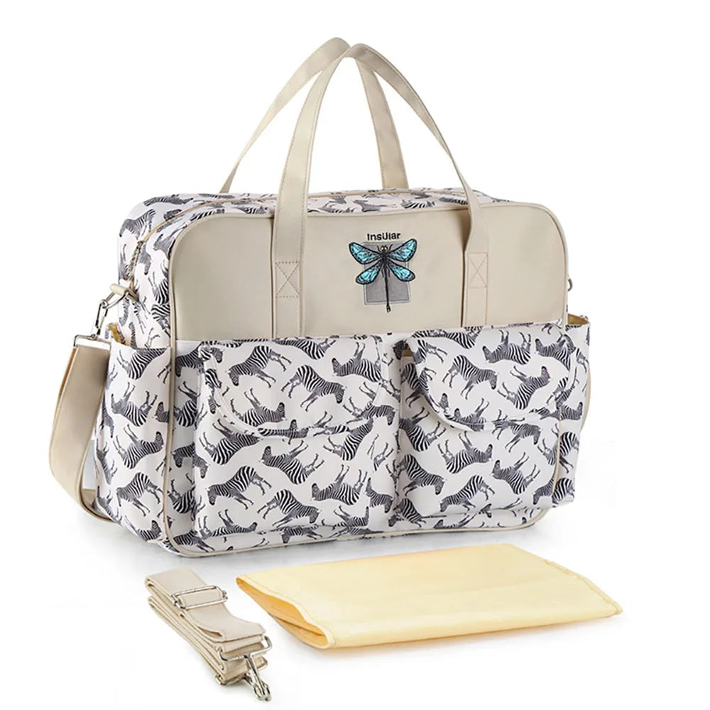 Bolsa maternidade estruturada bege com estampa de zebra, libélula bordada e trocador amarelo claro.