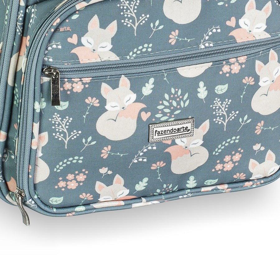 Detalhe aproximado de bolsa cinza-azulada com estampa de raposas, flores e zíper frontal.