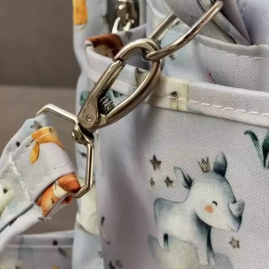Detalhe aproximado do fecho metálico prateado na alça da bolsa cinza com estampa safari
