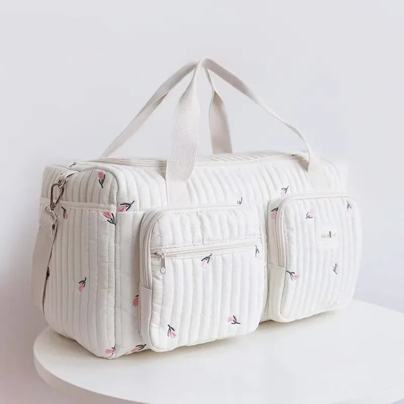 Bolsa maternidade off-white acolchoada com bordados florais em ângulo de três quartos.