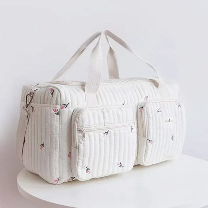 Bolsa maternidade off-white acolchoada com bordados florais em ângulo de três quartos.