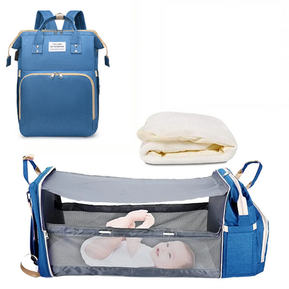 Mochila maternidade azul fechada, colchonete branco e berço portátil aberto com bebê deitado.