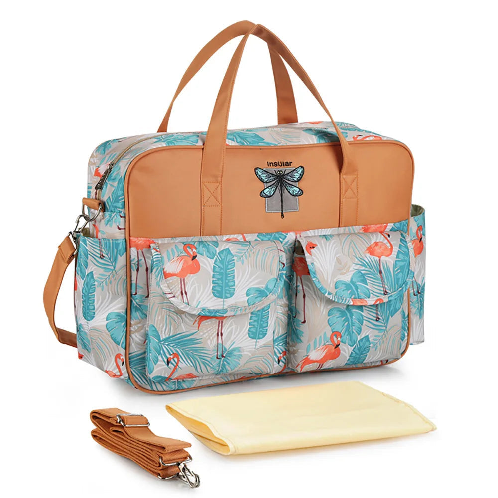 Bolsa de maternidade com estampa de flamingos, alças marrons, trocador amarelo e alça transversal.