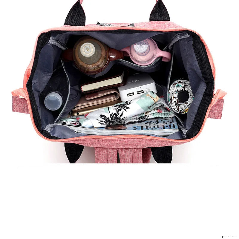 Vista aérea de mochila rosa aberta revelando o interior cinza organizado com diversos objetos.
