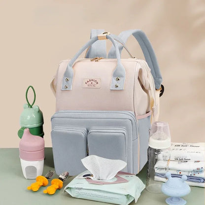 **Alt Text:** Mochila maternidade multifuncional impermeável rosa e azul-claro, vista frontal com acessórios de bebê.