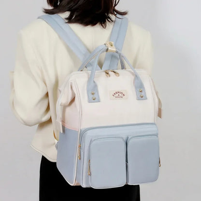 **Alt Text:** Mochila maternidade multifuncional azul pastel e creme, vista de costas em uma modelo.
