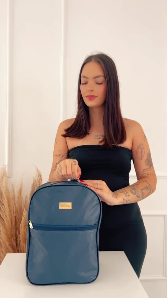 Mochila de maternidade azul-escura com detalhes dourados vista de frente sobre mesa branca.