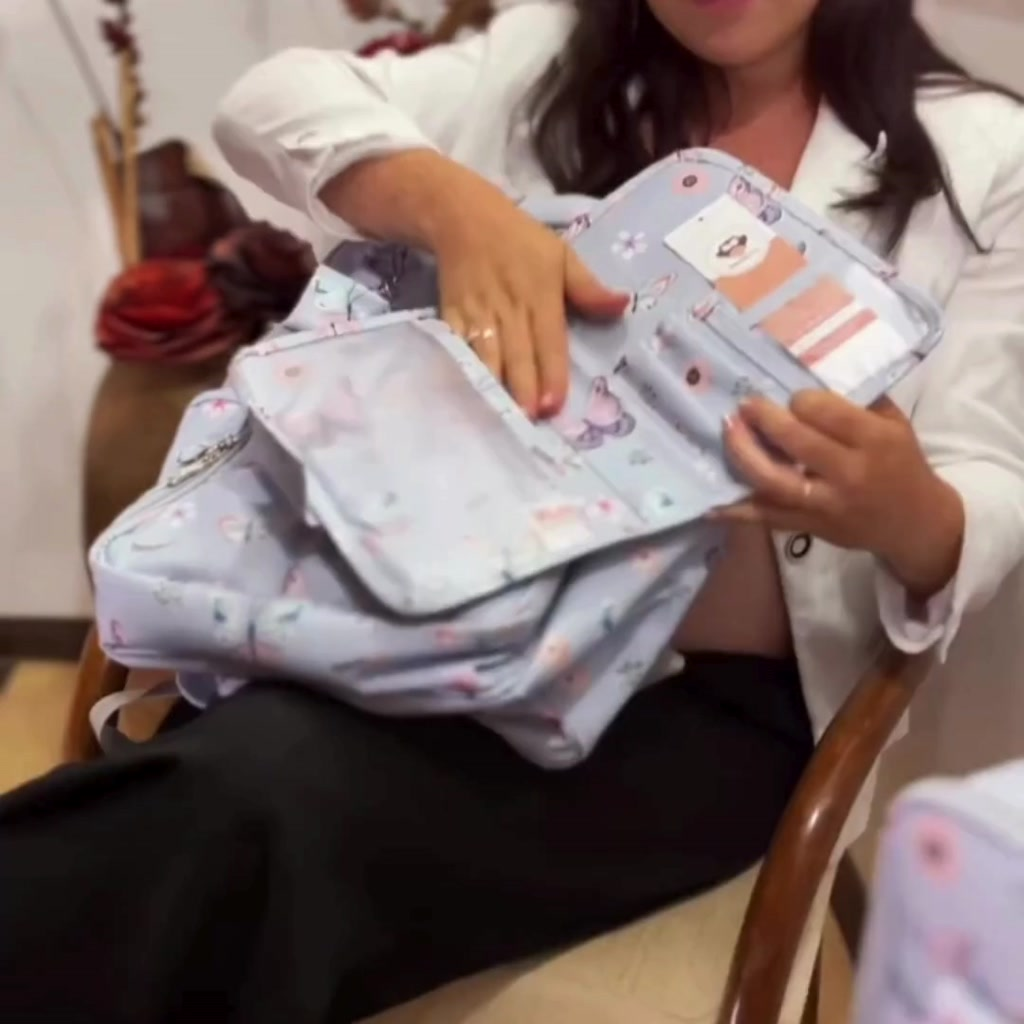 Bolsa de maternidade azul-clara com estampa de borboletas aberta, mostrando seus compartimentos internos.