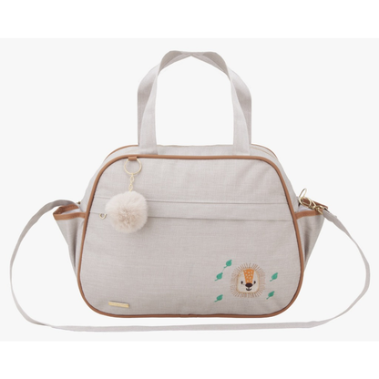 Bolsa de maternidade bege com bordado de leão, detalhes marrons, alças e chaveiro pompom.