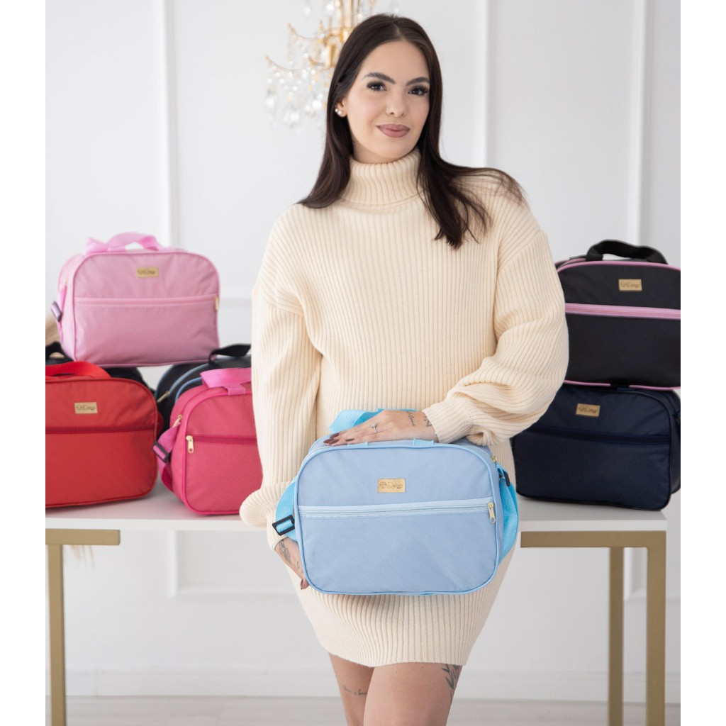 Mulher segura bolsa compacta azul-clara, com outros modelos coloridos expostos na mesa.