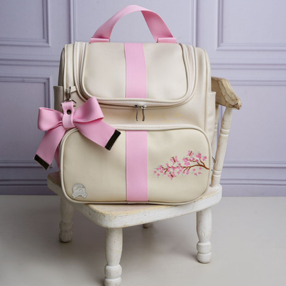 Vista frontal de mochila de maternidade bege estruturada, com detalhes rosa e bordado floral.