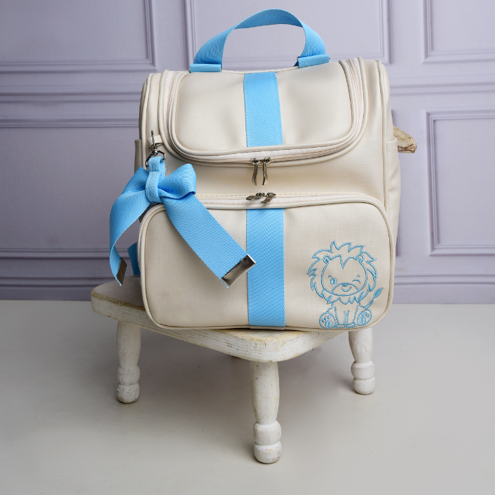 Vista frontal de mochila bege com detalhes, laço e bordado de leão em azul-claro.