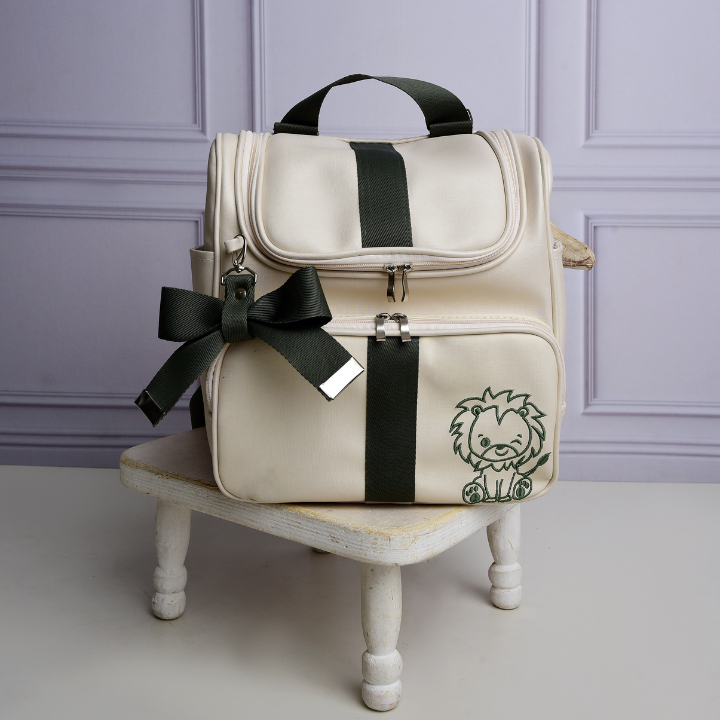 Mochila de maternidade bege com detalhes verdes e leão bordado vista de frente.