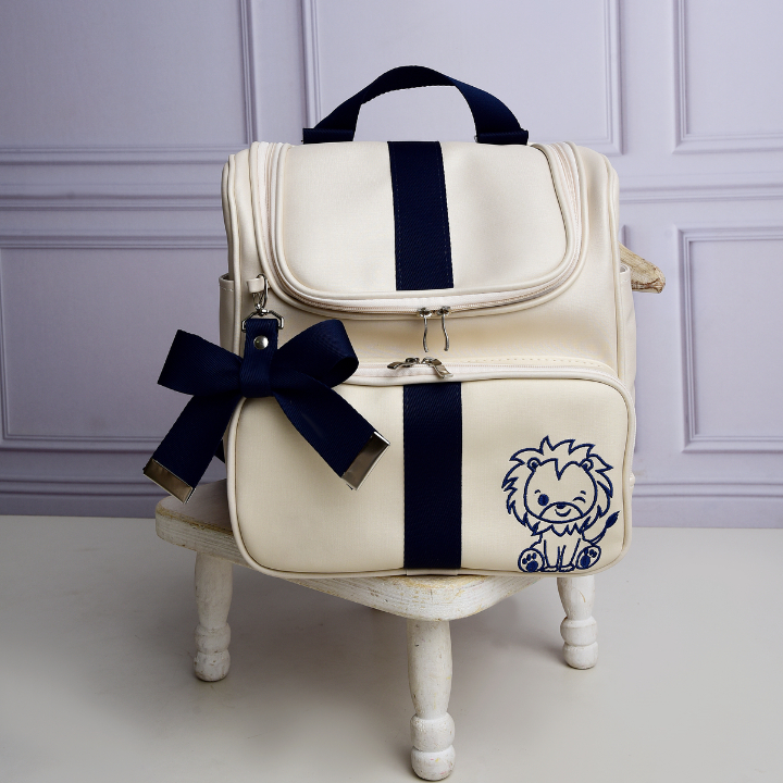 Mochila de maternidade creme com detalhes em azul-marinho e bordado de leão de frente.