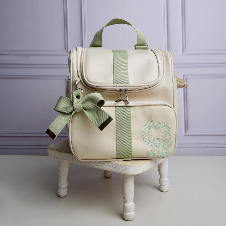 Mochila de maternidade bege com detalhes verdes e bordado de leão, vista frontal.