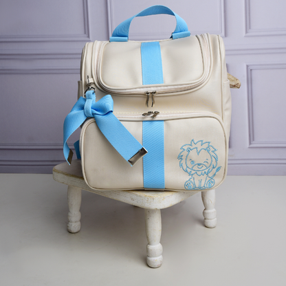Mochila bege com detalhes azul-claro e bordado de leão, apoiada sobre banqueta branca.
