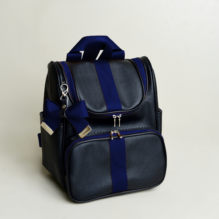 Mochila preta estruturada com detalhes em azul e laço decorativo sobre fundo claro.