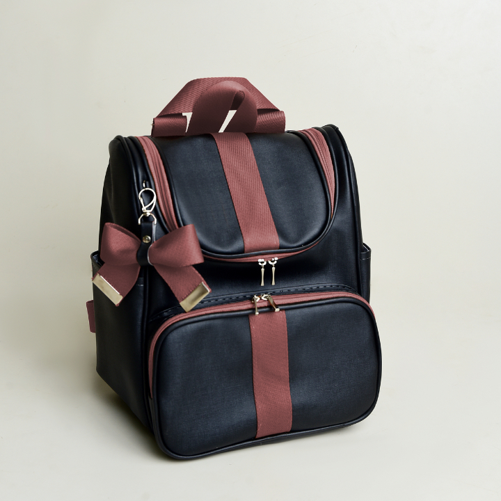 Mochila preta com detalhes marrons e laço lateral, vista em ângulo sobre fundo claro.