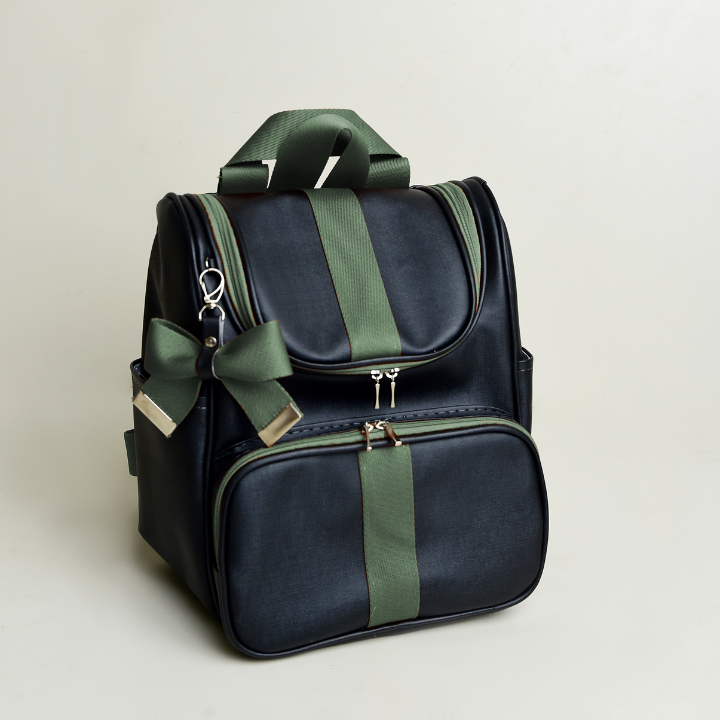 Mochila preta estruturada com detalhes e laço verdes, fotografada em ângulo de três quartos.