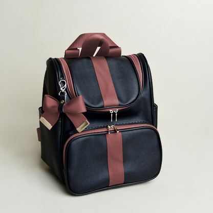Mochila preta estruturada com faixas e laço marrons, fotografada em ângulo sobre fundo claro.