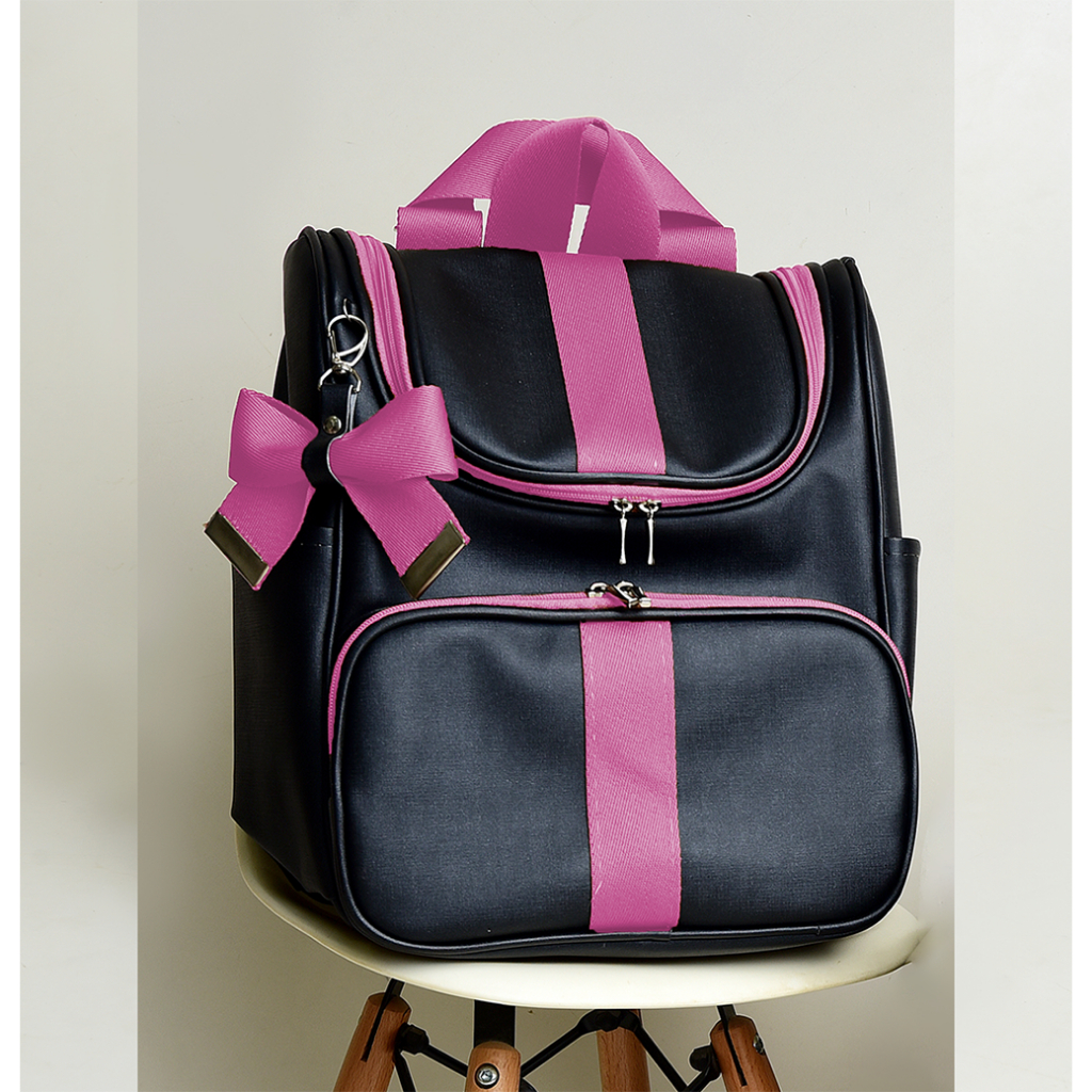 Mochila preta com detalhes e laço rosa, fotografada de frente sobre uma cadeira.