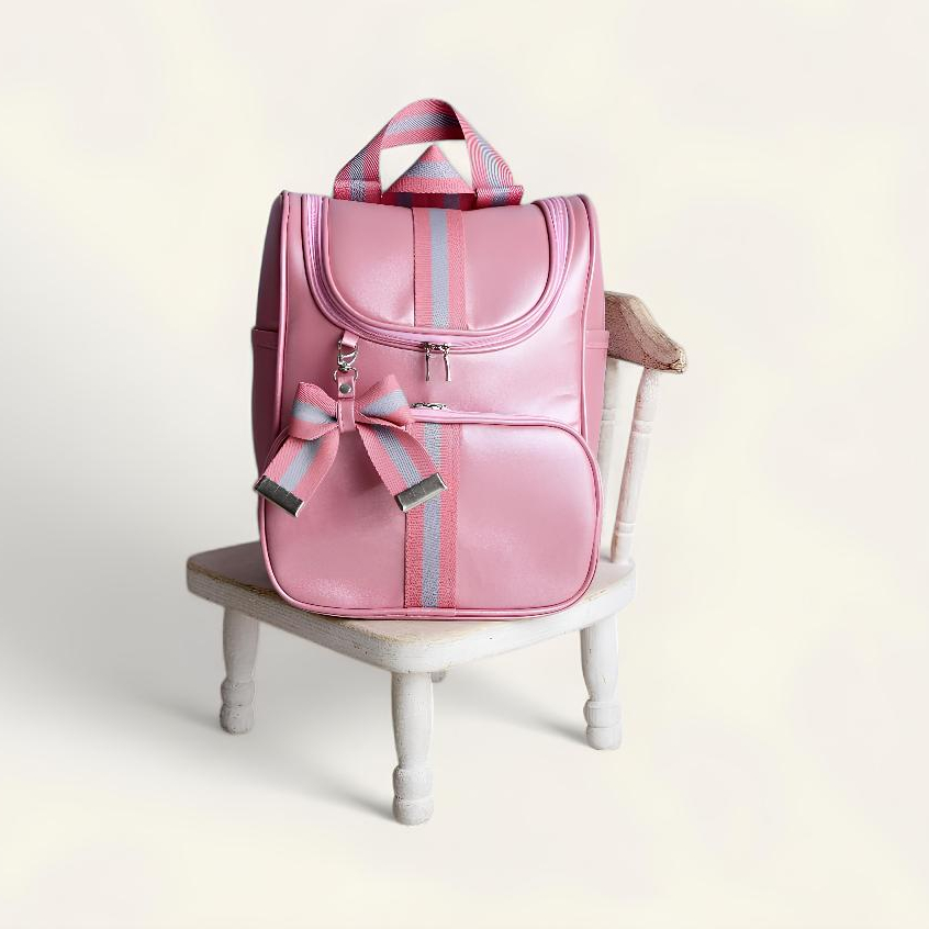 Mochila rosa com laço e listras cinzas, vista de frente sobre uma cadeira branca.
