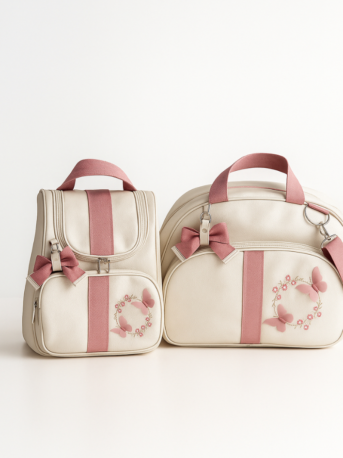 Vista frontal de mochila e mala maternidade bege e rosa com bordados de borboletas.