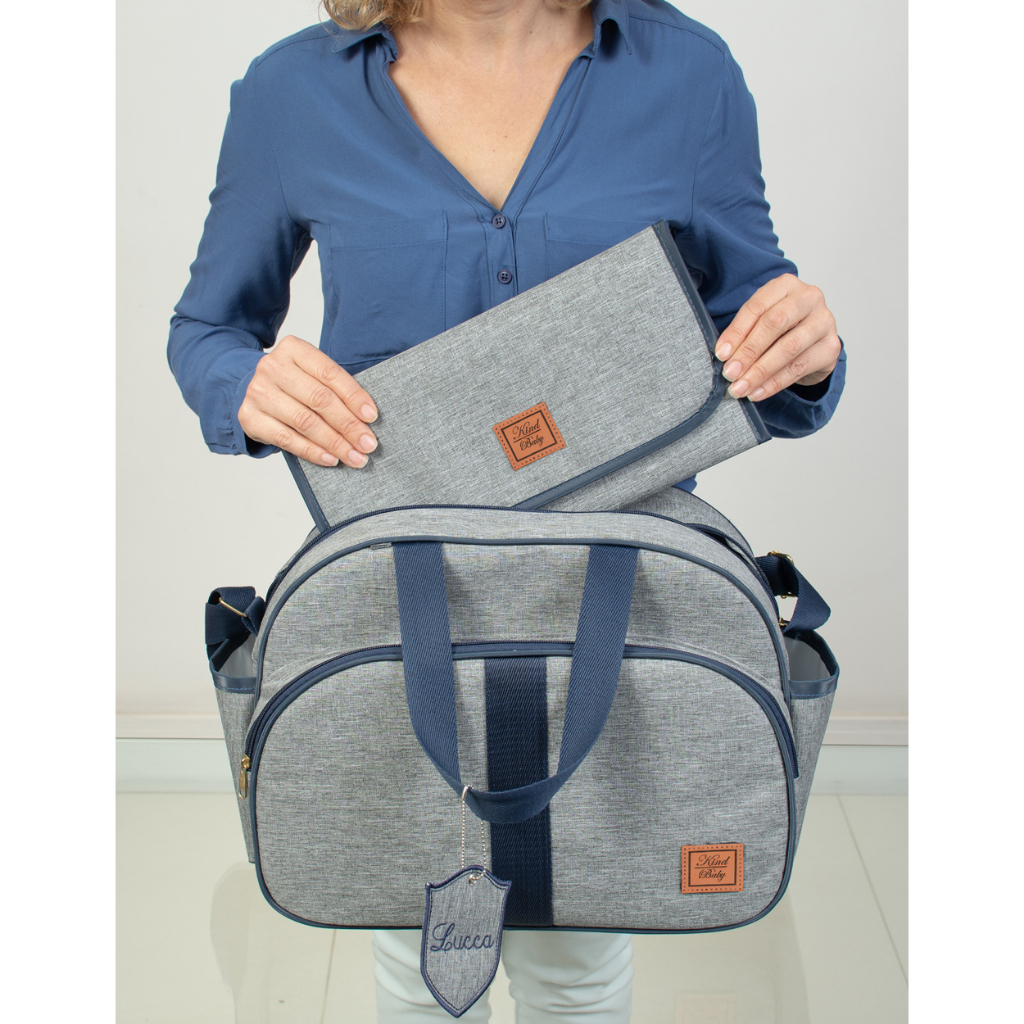 Bolsa de maternidade cinza com detalhes azuis, trocador e chaveiro personalizado em vista frontal.