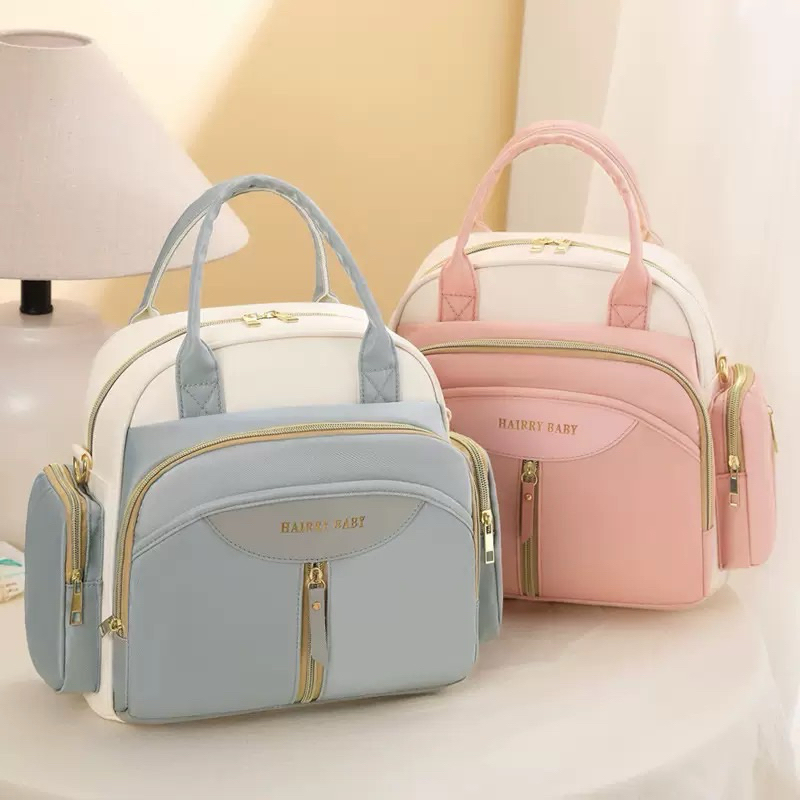 Duas bolsas de maternidade estruturadas, azul e rosa pastel, com detalhes em dourado.