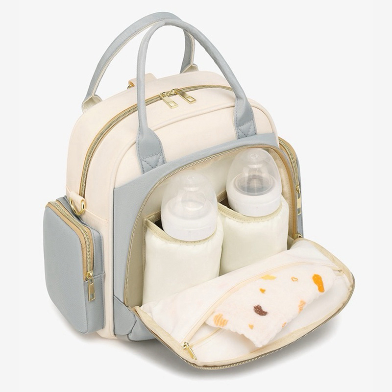 Mochila maternidade bege e azul-claro, vista diagonal, com bolso frontal aberto contendo mamadeiras.