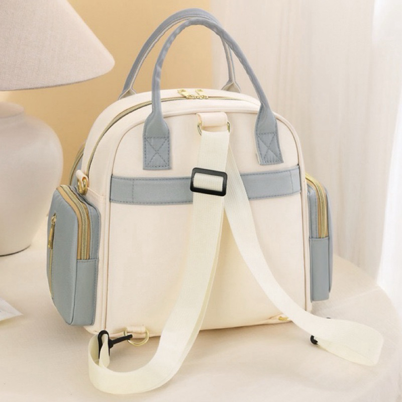 Vista traseira de mochila maternidade nas cores creme e azul com alças brancas.