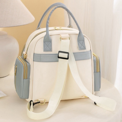 Vista traseira de mochila maternidade nas cores creme e azul com alças brancas.