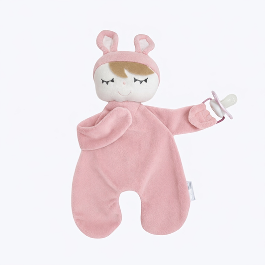 Naninha de pelúcia rosa com orelhas de coelho segurando chupeta em fundo branco.