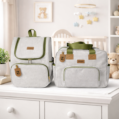 Mochila e bolsa de maternidade cinza com detalhes verdes sobre uma cômoda branca.