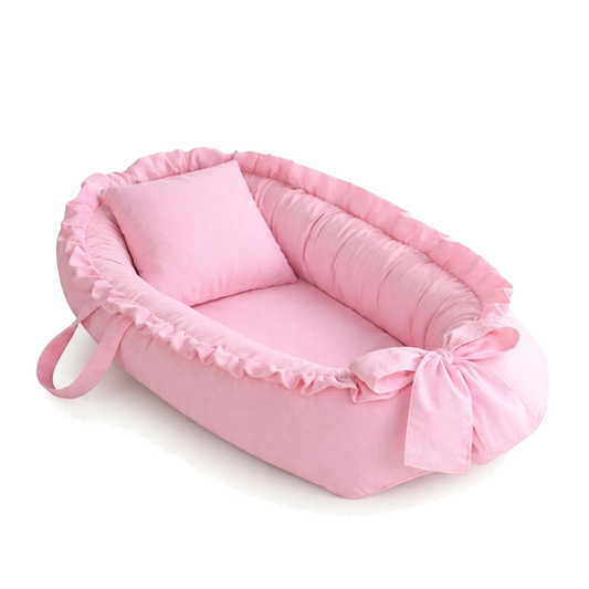 Ninho de bebê oval rosa com travesseiro e laço, visto em ângulo diagonal elevado
