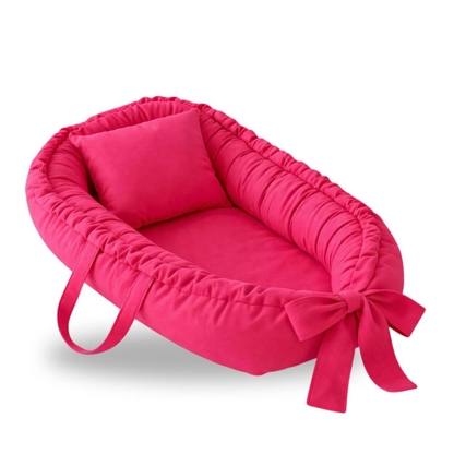 Ninho redutor de berço rosa vibrante com travesseiro e laço, em perspectiva diagonal.