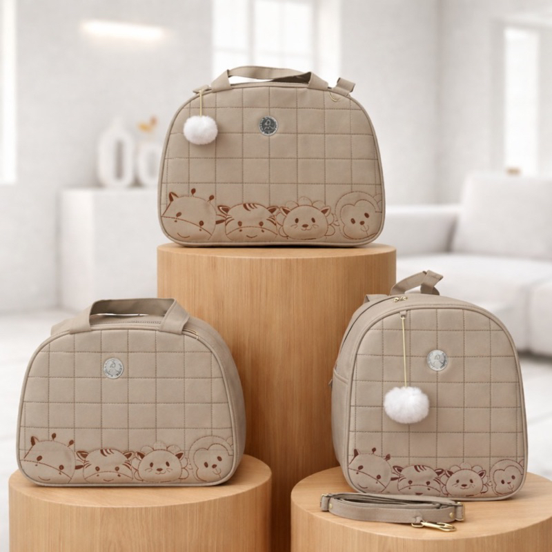 Três bolsas de maternidade bege com bordados de animais sobre pedestais cilíndricos de madeira.
