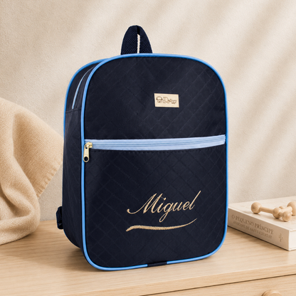 Mochila azul-marinho com bordas azul-claro e o nome Miguel bordado em dourado, vista frontal.