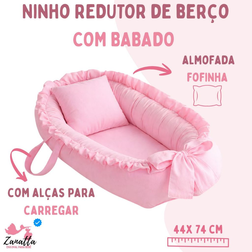 Ninho redutor de berço rosa com travesseiro e babados em vista diagonal elevada.