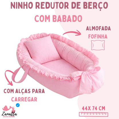 Ninho redutor de berço rosa com travesseiro e babados em vista diagonal elevada.
