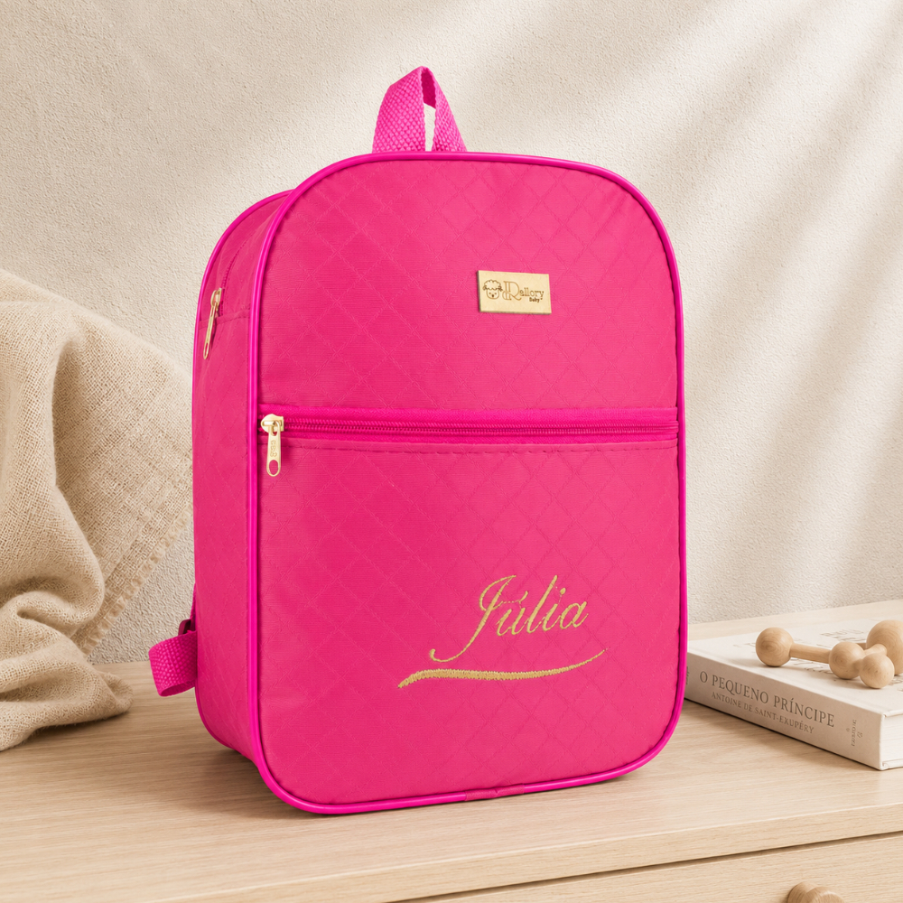 Mochila maternidade rosa com textura matelassê e o nome Júlia bordado em dourado.