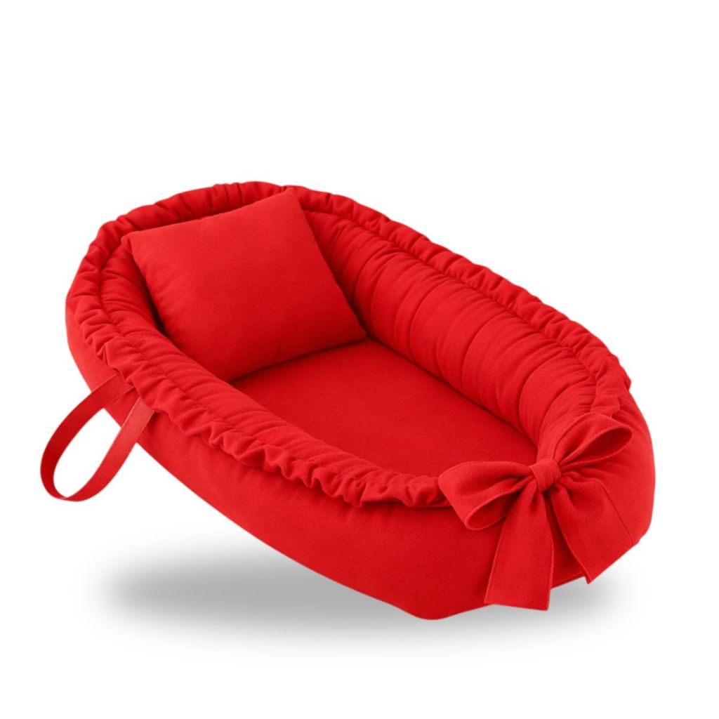 Ninho de bebê vermelho oval com travesseiro e laço em perspectiva inclinada.