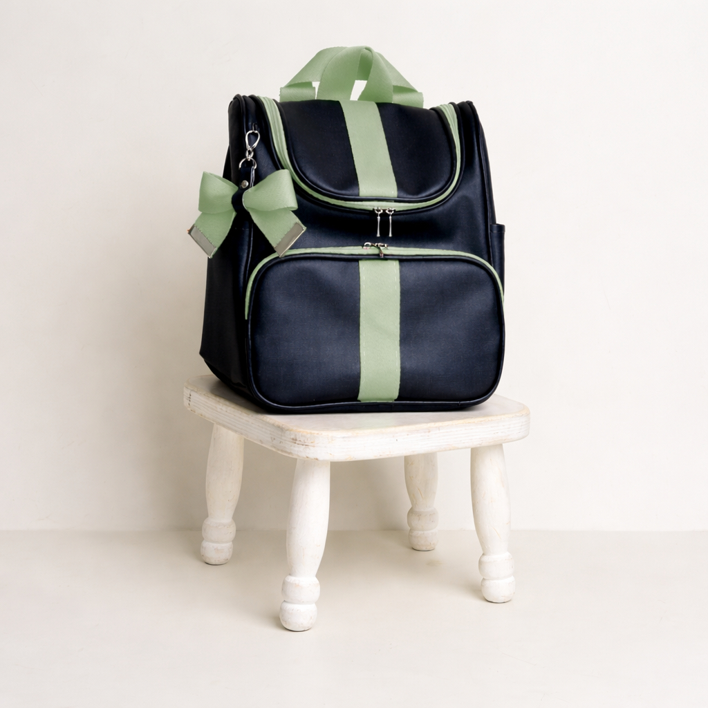 Mochila preta com detalhes verde-claro sobre pequeno banco de madeira branco.