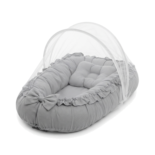 Ninho de bebê oval cinza com mosquiteiro e travesseiro, em ângulo no fundo branco.