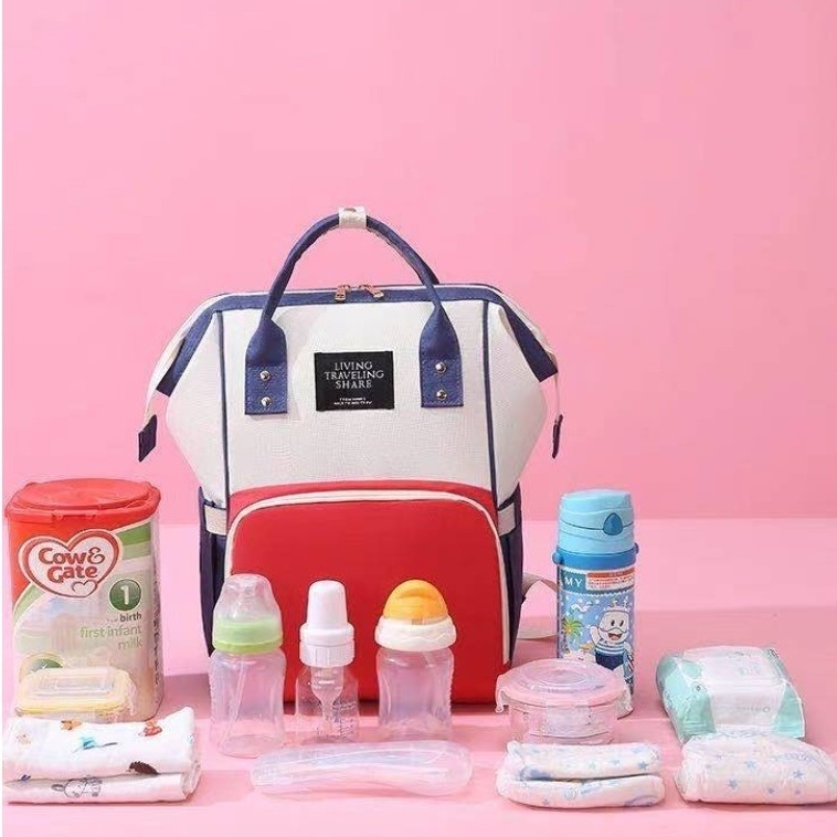 Mochila maternidade tricolor centralizada com acessórios de bebê sobre fundo rosa, vista frontal.