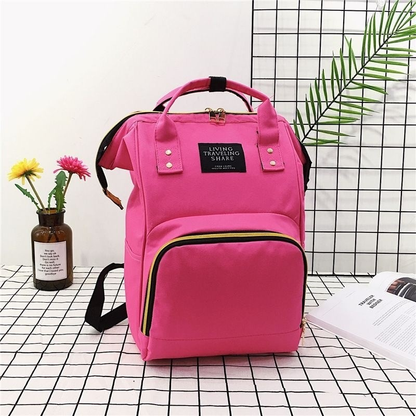 Mochila maternidade rosa vibrante estruturada em ângulo frontal sobre superfície quadriculada.