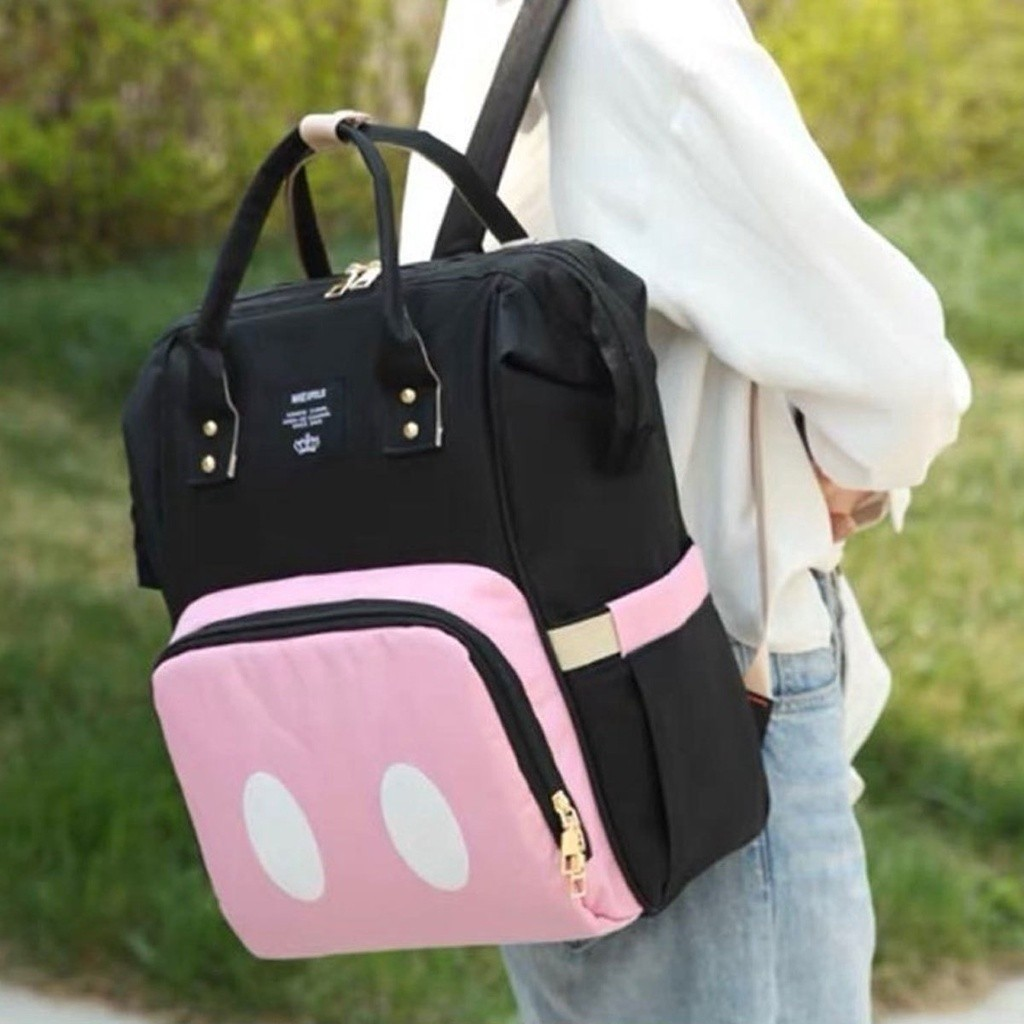 Mochila de maternidade preta e rosa com círculos brancos, vista de perfil em uso.