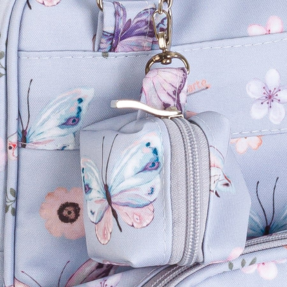 Detalhe em close de pequeno estojo cúbico estampado com borboletas pendurado em mochila azul-claro.