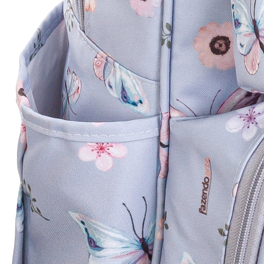 Detalhe em close de bolso de mochila lilás com estampa de flores e borboletas.