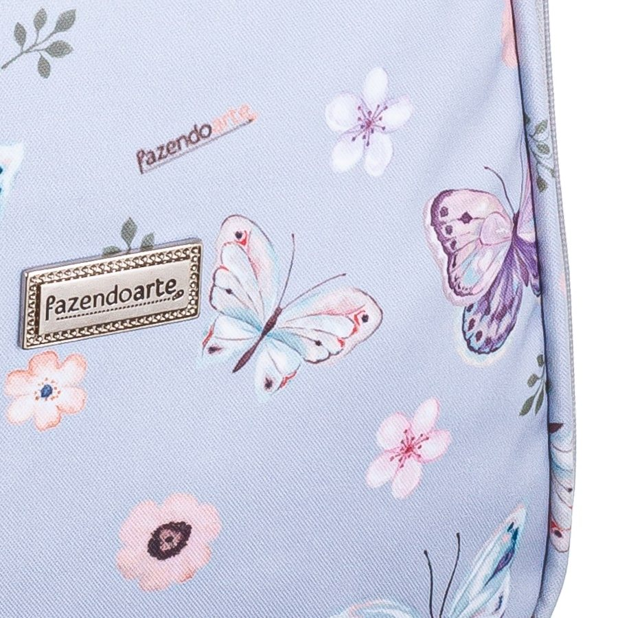 Detalhe de tecido azul-claro com estampa de borboletas, flores e placa de metal.